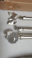Close-up showing champagne leaf-shaped finials on one rod and crystal ball finial on the other rod in matte silver finish.