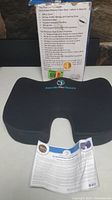 Black gel-infused memory foam seat cushion with ergonomic U-shaped cutout shown front side with instruction pamphlet and original packaging.