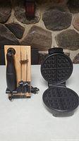 Oster electric carving tool with wooden stand and three stainless steel blades next to Oster waffle maker opened to show non-stick plate grid pattern.