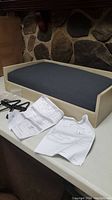Photo of unassembled pet bed frame with gray cushion on top, assembly instructions and tools included.