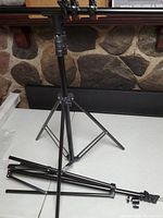 Photo showing the metal T-stand backdrop stand assembled with three spring clamps holding the horizontal bar, set against a stone background.