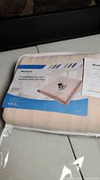 Plastic-wrapped twin size heated mattress pad in beige with product label showing product name and image of mattress pad and remote.