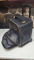 Side view of black wheeled pet carrier with retracted handle, expandable mesh compartment open showing ventilation mesh on sides