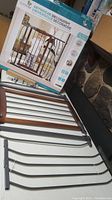 Photo of the new safety gate unassembled next to its slightly distressed box showing a wood and metal frame with installation accessories.