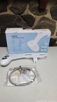 Photo of YASFEL bidet attachment in front of product box. Box is white and blue with product image and features printed. Device is white plastic with two control dials.