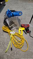 Photo of Senco air compressor with attached blue coiled hose, Skill drill and Stanley stapler along with yellow extension cord and manual.