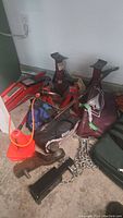 Wide shot of lot showing hydraulic trolley jack, four jack stands, tow posts, emergency kit bag, tire chains, and assorted tools on garage floor.