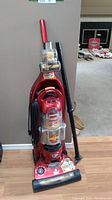 Full front view of the upright red Bissell vacuum cleaner with cord wrapped and an accessory wand attached to the side.