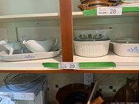 Shelf displaying a variety of kitchenware including CorningWare Cornflower blue pieces, French white casseroles, and Glassbake dishes.