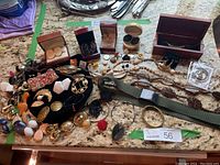 Wide view of entire collection spread on countertop showing earrings, bracelets, necklaces, belt, and jewelry boxes