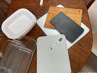 Four cutting boards of varied types and sizes on a table, including large glass, wooden, ridged black, and glass boards.