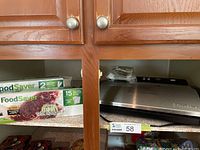 Photo showing FoodSaver heat seal rolls and pre-cut bags packaging on shelf next to sealed vacuum sealer device.