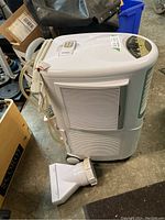 Front and side view of the white ForestAir portable air conditioner with exhaust hose adapter attached and remote control slot visible on top.