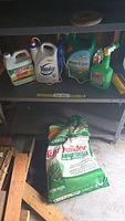 Bottom shelf with large green Scotts Turf Builder Fertilizer bag resting against back wall with wood framing partially visible.