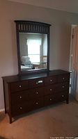 Front angle view of the dresser with mirror reflecting a window and chair.