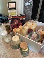 Overview of large assortment of candles and candle holders with boxed candle set in background.
