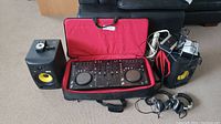 Wide shot of Pioneer DJ controller in red-lined soft case alongside two KRK Rokit 6 speakers with yellow cones, headphones and cables