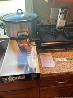 Crock-Pot slow cooker with glass lid on kitchen counter next to Salton Hotray box and Cassia oil spray pump.