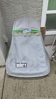 Weber branded protective cover for the fireplace, grey fabric with some dirt marks and sticker tag.