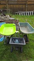 View of all three items: bright light green plastic wheelbarrow, light blue plastic wheelbarrow, and black plastic fertilizer spreader, showing condition and features.