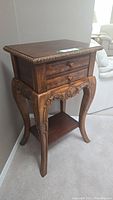 Side angled view of wooden French style side table with two drawers and carved legs