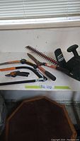 Wide view of the multiple yard tools including the Yardworks trimmer, bow saw, pruners, and crosscut saw on a white surface.