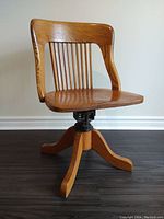 Front view of vintage oak bankers desk chair, showing curved backrest, vertical slats, contoured seat and four-leg base with swivel mechanism.
