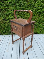 Front side of Victorian smoking stand showing the box body, turned legs, carved top handle, and front hinged door with round knob and carved detailing.