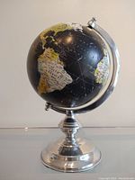 Front view showing the globe on polished aluminum base with black ocean and yellow-white landmasses