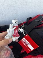 Coca-Cola polar bear Christmas ornaments with tags visible, held over top of red and black Coca-Cola duffle bag.