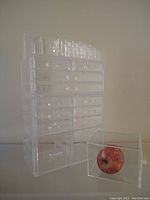 Clear acrylic stacking storage drawers with multiple drawers and compartments, one drawer pulled out showing size using an apple for scale.