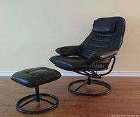 Full view of black leather recliner chair and matching ottoman angled side by side on wood floor against plain wall