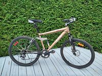 Full side view of the CCM men's mountain bike showing bronze and black frame, tires, and suspension.