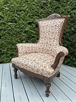 Full view of antique parlour chair showing floral upholstery, carved wooden frame, and overall shape.