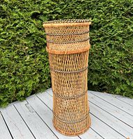 Full front view of the cylindrical woven rattan plant stand with lattice work and black accent wraps, showing the entire height and shape.