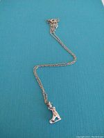 Full view of silver chain necklace with ice skate charm pendant resting on a turquoise surface.