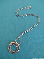 Silver chain necklace laid out on a teal background showing the pendant with 'LOVE' engraving on the front side of the circular ring pendant.