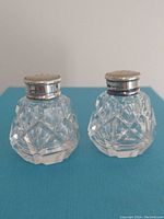 Front view of both shakers showing the cut glass body and silver tops.