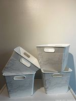 Four white plastic storage bins stacked, showing marble print and oval handles on all sides.