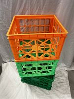 Stack of three large plastic storage crates, one orange on top of two green ones, all with open grid design.