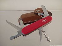 Swiss Army multi tool displayed with most fold-out tools visible: saw blade, screwdriver/can opener, large blade, corkscrew, and smaller blade.