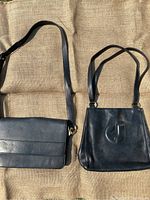 Two black leather purses side by side on textured fabric background, showing shape and straps