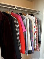 Side view of various vintage women's jackets and blouses hanging on a rack showing different colors and patterns including houndstooth and floral prints.