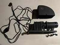 Front view of vintage camera with attached wires and detachable cover placed nearby on white surface.