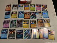 Top view of approximately 25 Pokemon cards arranged in rows, many holographic including Charizard and legendary Pokemon cards.
