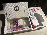 Set displayed in white holographic box with Pokemon logo, showing the contents inside including dice, playmat, counters, and cards.