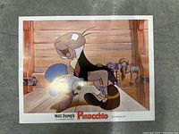 Photo of a vintage lobby card showing Geppetto and Jiminy Cricket inside a wooden room from Disney's Pinocchio.