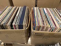 Two cardboard boxes filled with approximately 120 vinyl records standing vertically, showing the spines and edges of album covers.