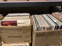 Two cardboard boxes labeled 17 and 18 filled with assorted vinyl records.