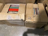 Two cardboard boxes labeled 25 and 26 with mixed vinyl records inside, partially visible cover colors include red and green.